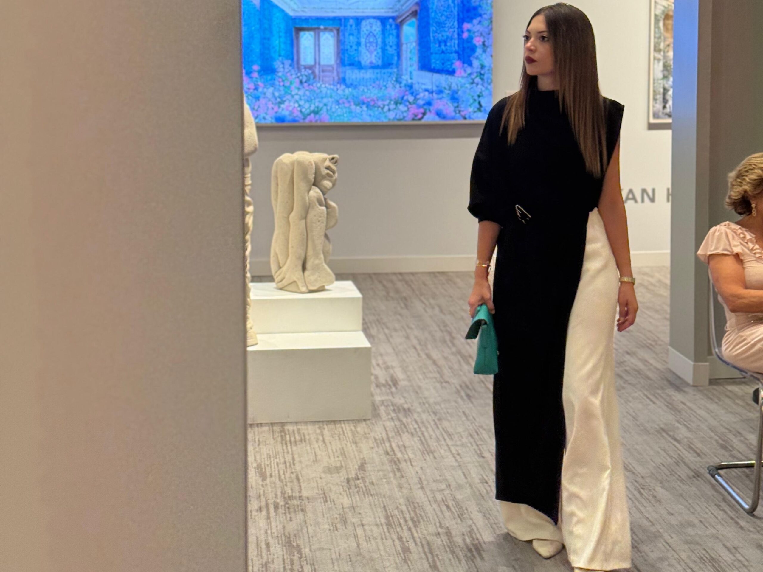 A stylish woman in a black and white evening outfit walks through Contemporary Istanbul, observing sculptures, digital artworks, and gallery displays as part of the process of discovering personal taste before starting an art collection.
