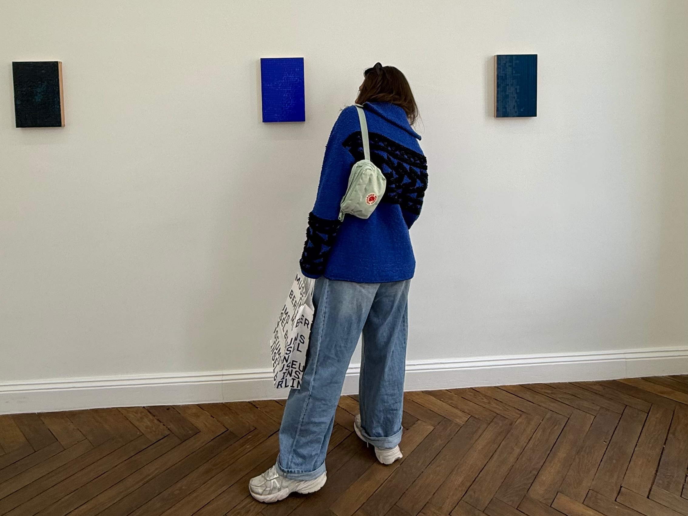 gırl lookıng at artworks
A gallery visitor in a blue sweater and wide-leg jeans looks closely at contemporary blue artworks in a minimal exhibition space, symbolizing the early stage of starting an art collection by learning how to observe, define personal taste, and connect emotionally with art before buying.